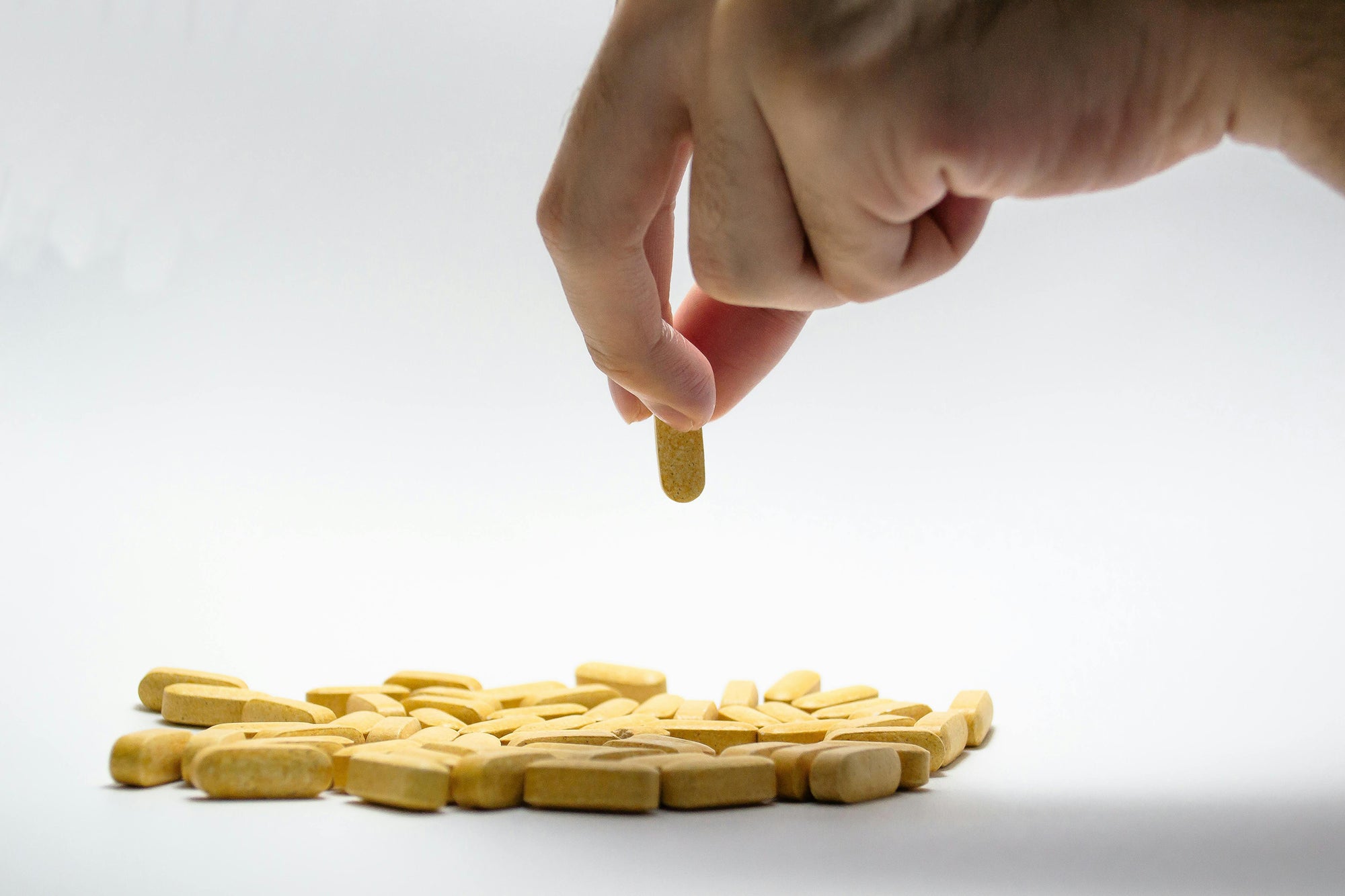 Hand placing a yellow pill on a pile of similar pills against a white background