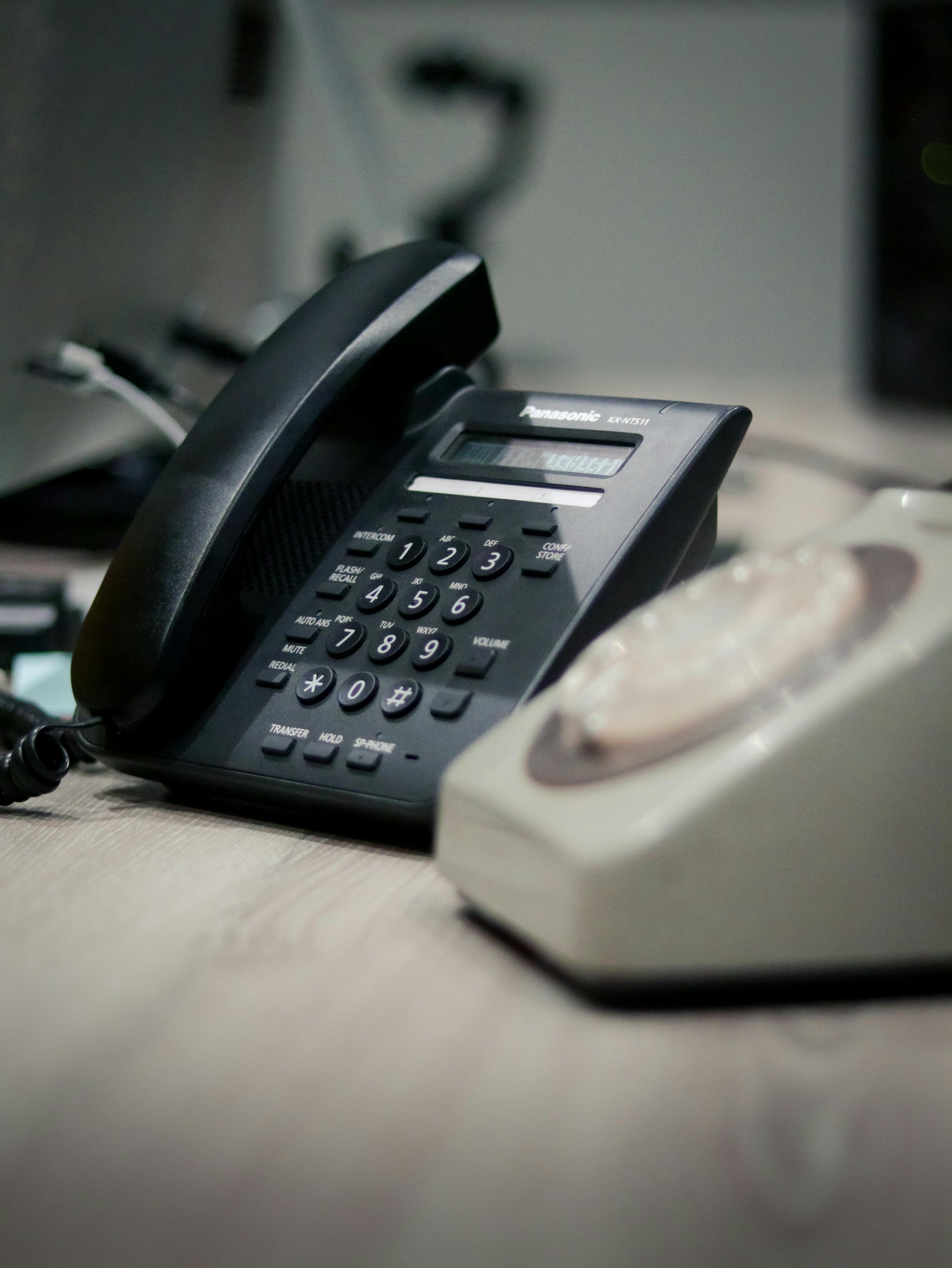 Black office phone and white landline phone on a desk